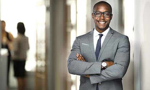 Man crosses his arms in a gray professional suit as he oversees project teams and interacts with industry stakeholders throughout the day.