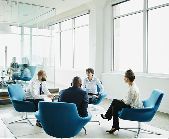 Four coworkers sit in blue, round chairs to discuss a project related to their critical industry experience with major media companies. Four coworkers sit in blue, round chairs to discuss a project related to their critical industry experience with major media companies.